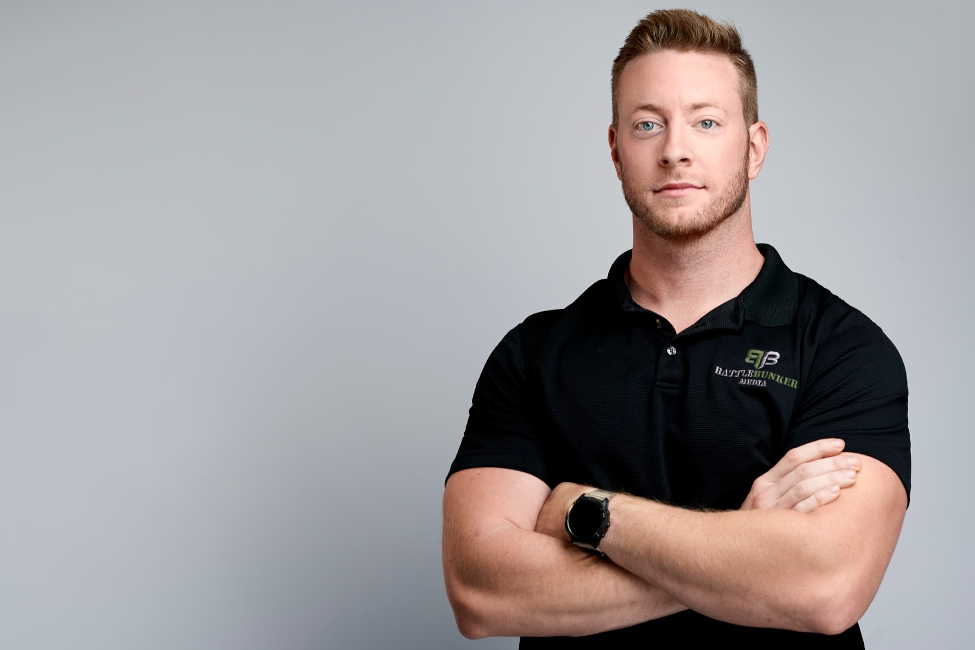 Austen Alexander in a black Battle Bunker Media polo with arms crossed against a gray background