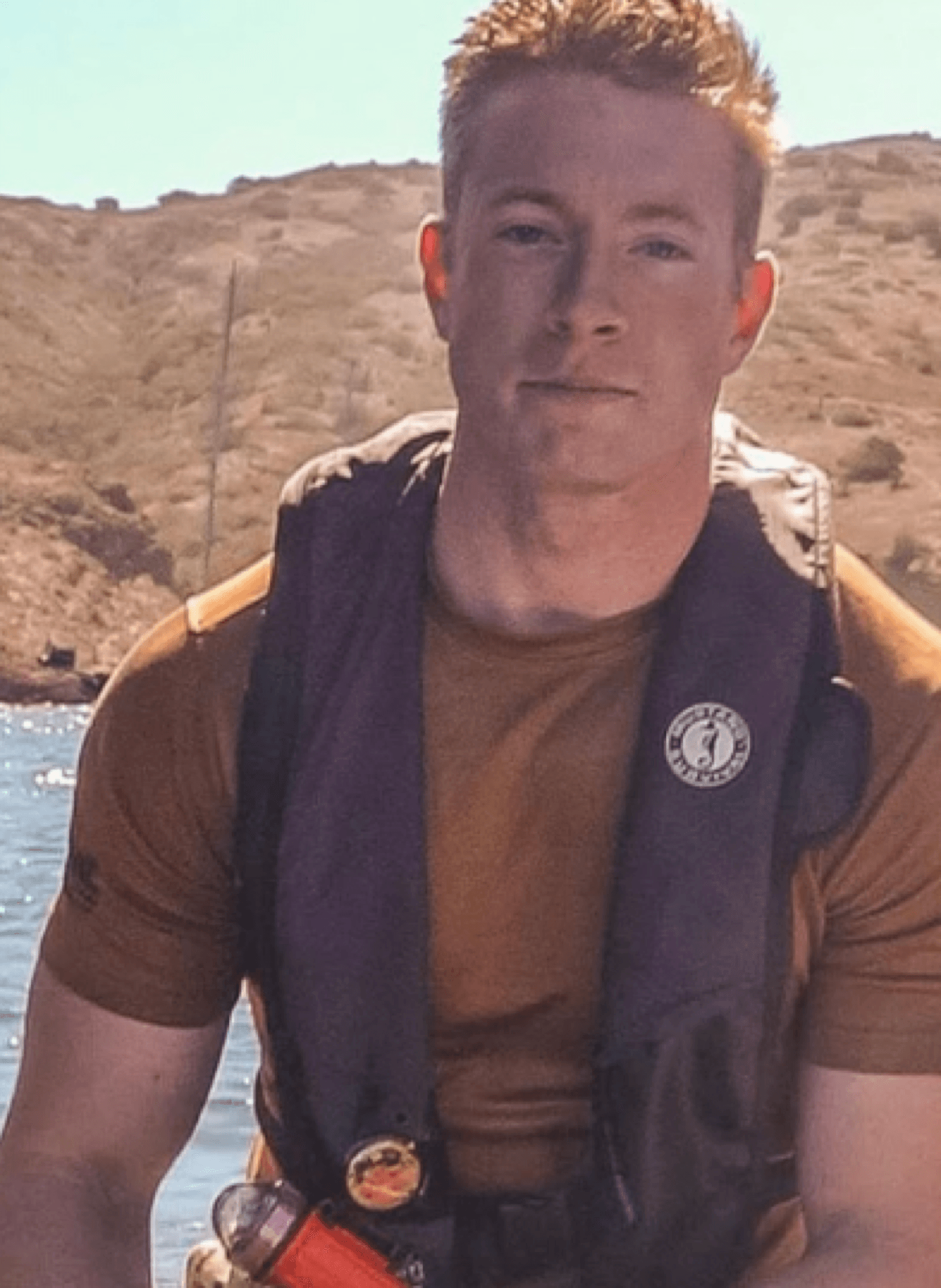 Austen Alexander on a boat wearing a life vest, with coastal hills in the background