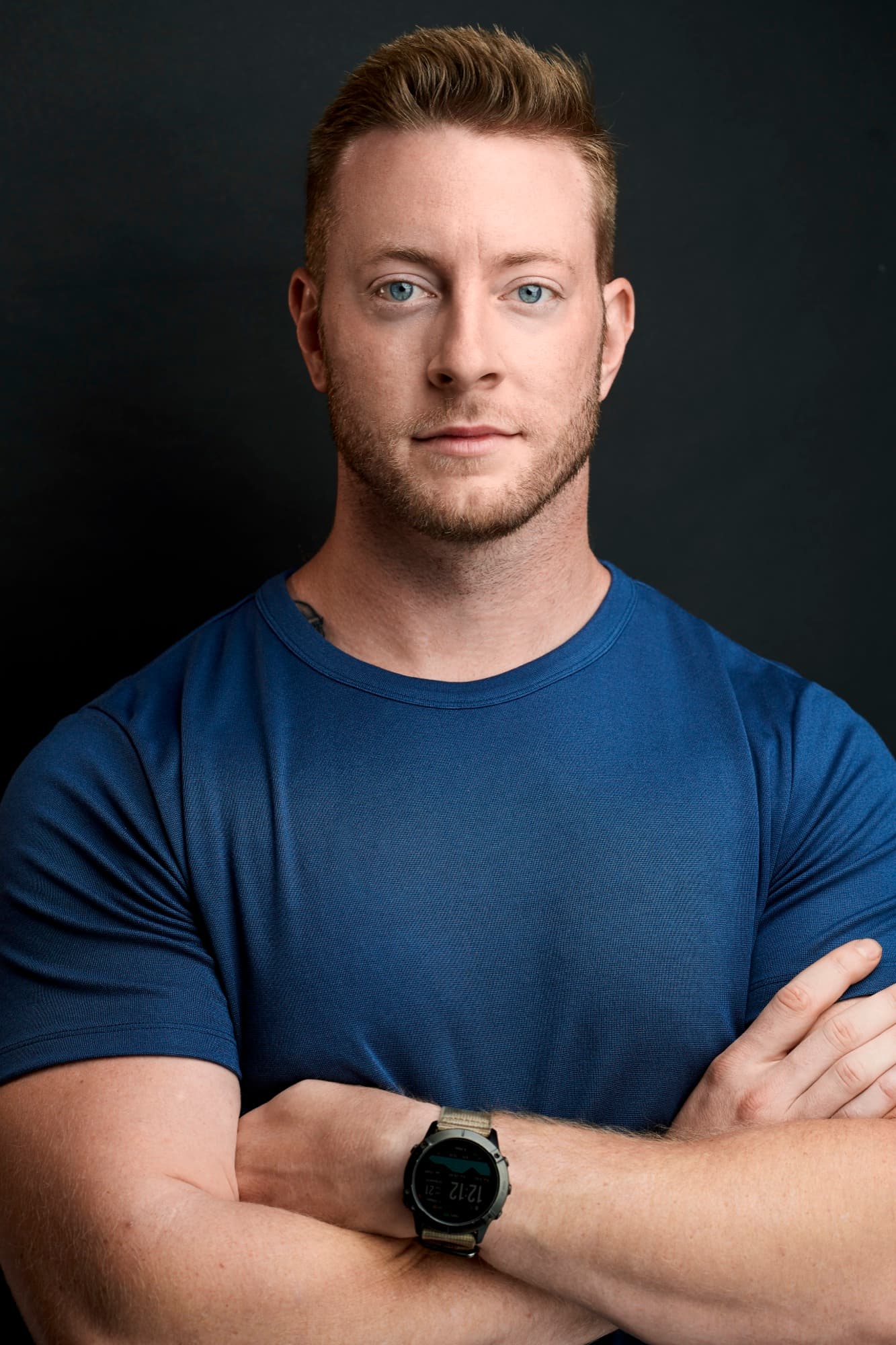 Austen Alexander with arms crossed in a navy blue t-shirt against a dark backdrop