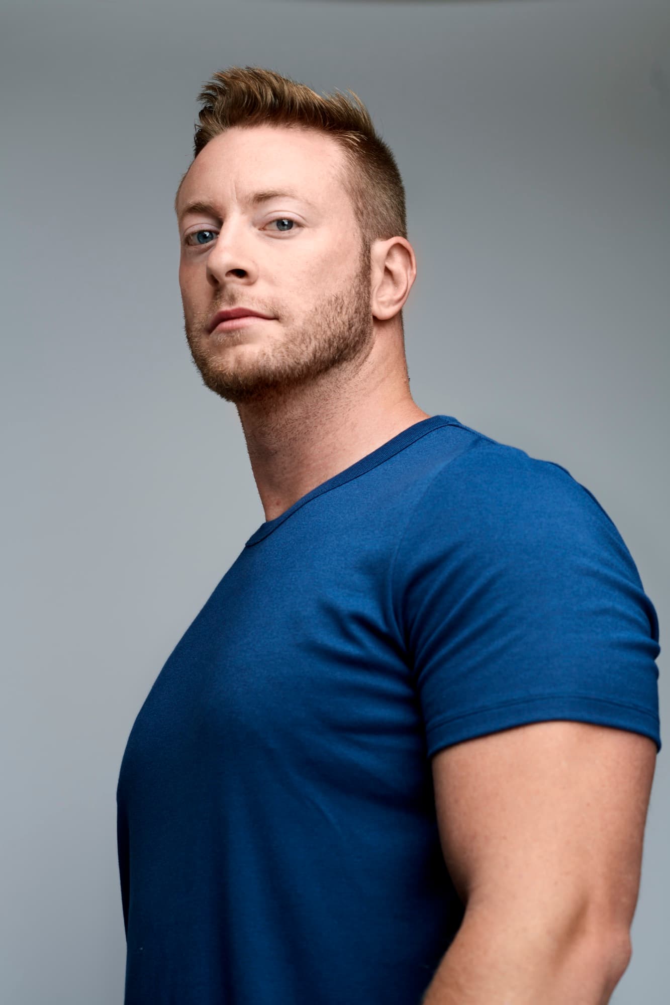 Austen Alexander in a blue t-shirt, three-quarter profile against a gray background